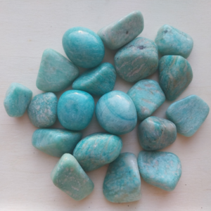 Pierres roulées d’amazonite aux reflets bleu-vert, polies et disposées sur une surface claire.