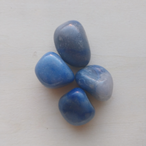 Quatre pierres roulées d’aventurine bleue, aux reflets doux et veinures claires, posées sur fond clair.