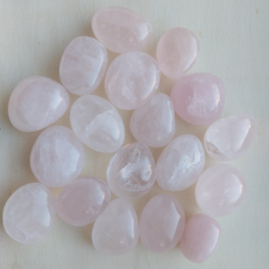 Pierres roulées de quartz rose, translucides et rosées, disposées sur une surface en bois clair.