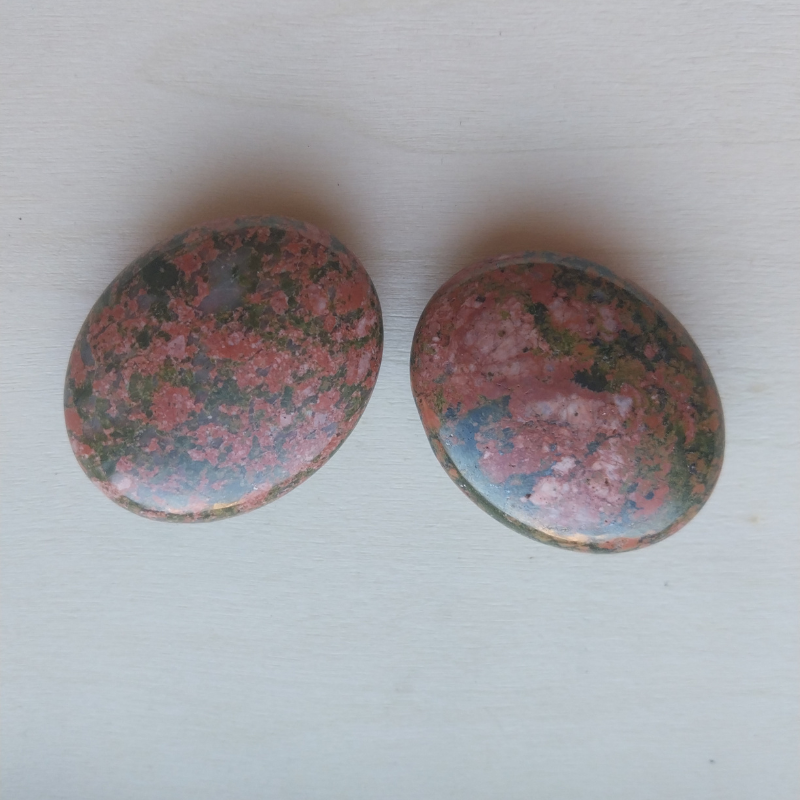 Deux galets d’unakite polis, aux teintes mêlées de vert, rose et noir, posés sur bois clair.
